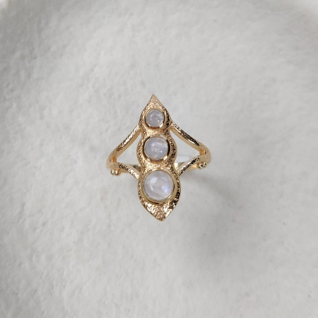 Gold ring with three moonstones on a textured white surface.