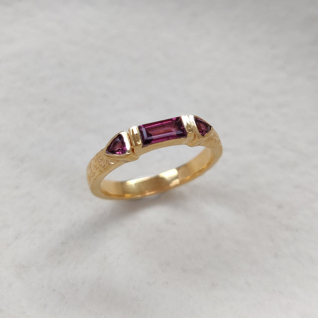 Gold ring with red purple gemstones on a white background