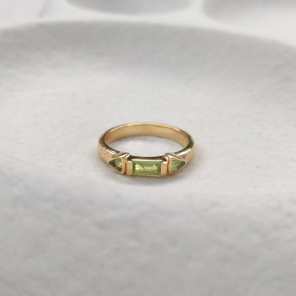 Gold ring with a green gemstone on a white stone surface