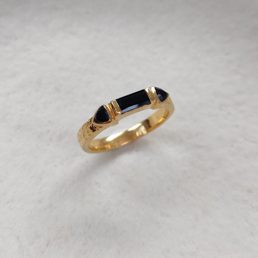 Gold ring with black onyx gemstones on a white ceramic dish