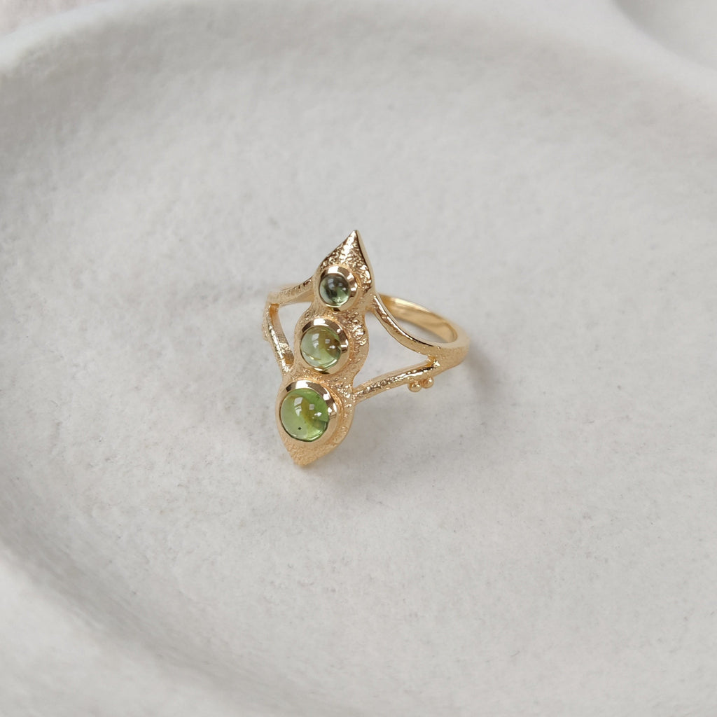 Gold ring with three green gemstones on a white plate.