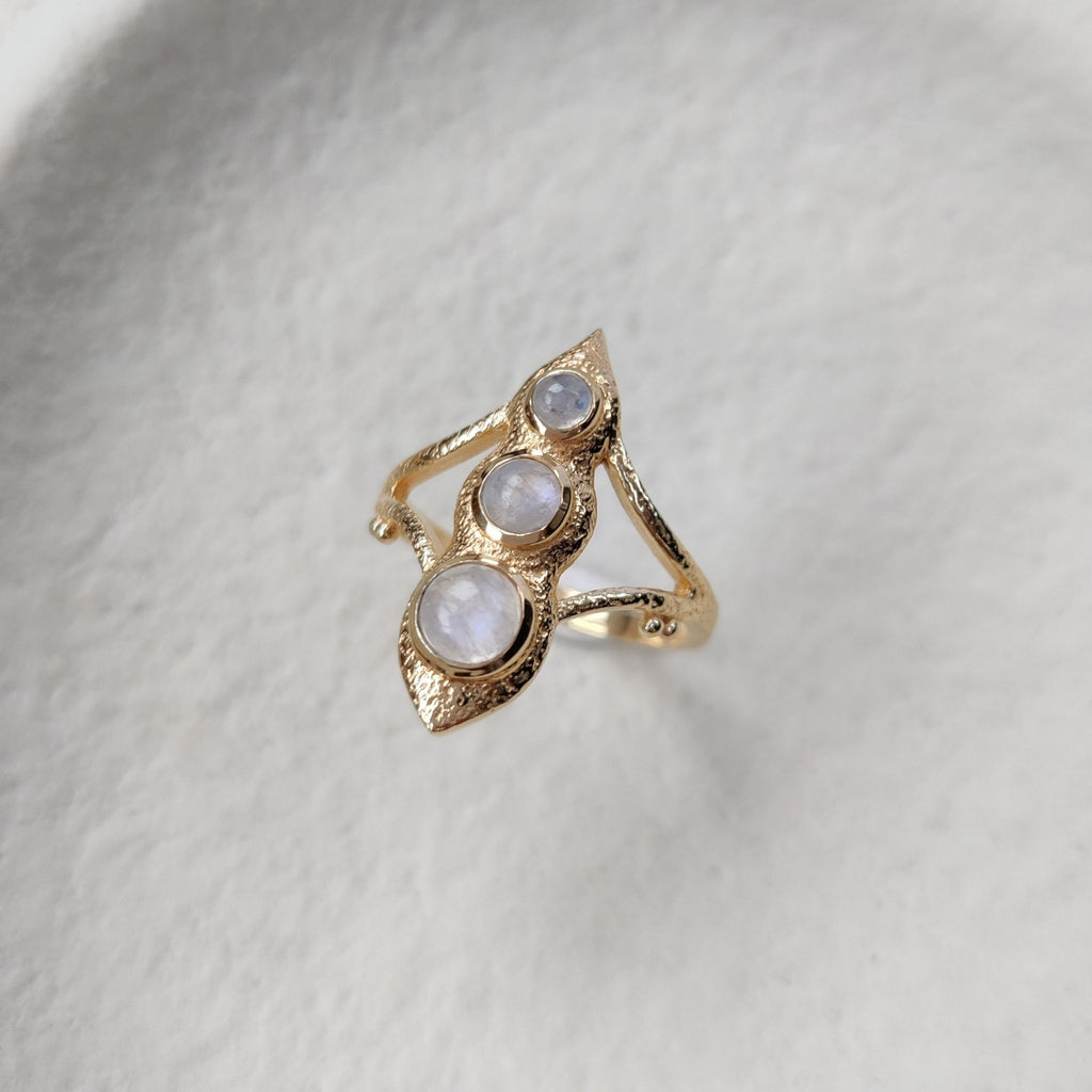 Gold ring with three round gemstones on a textured white surface