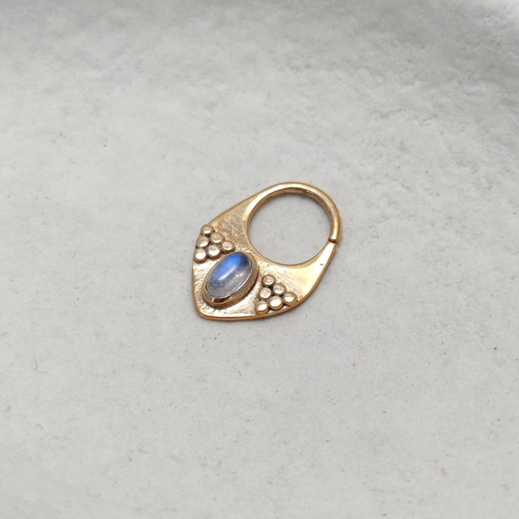 Triangle gold septum nose ring with moonstone, displayed on a jewelry dish.