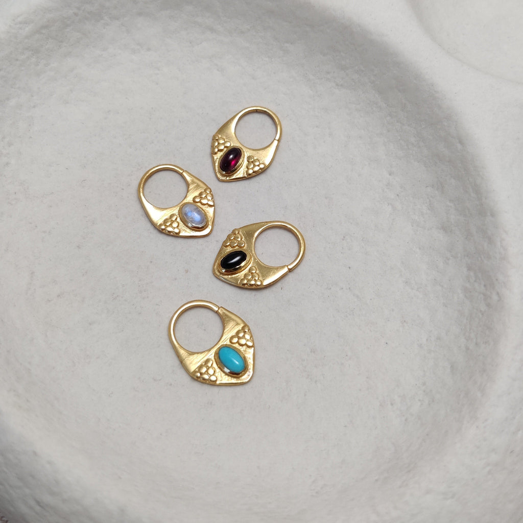 Close-up of gold septum nose rings with gemstones showcased from various angles, highlighting their intricate details and v-shape design.