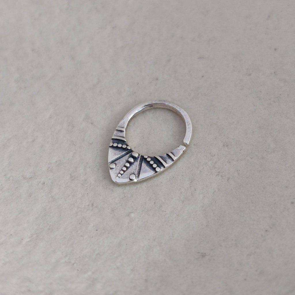 Silver nose ring with engraved design on a textured white surface.