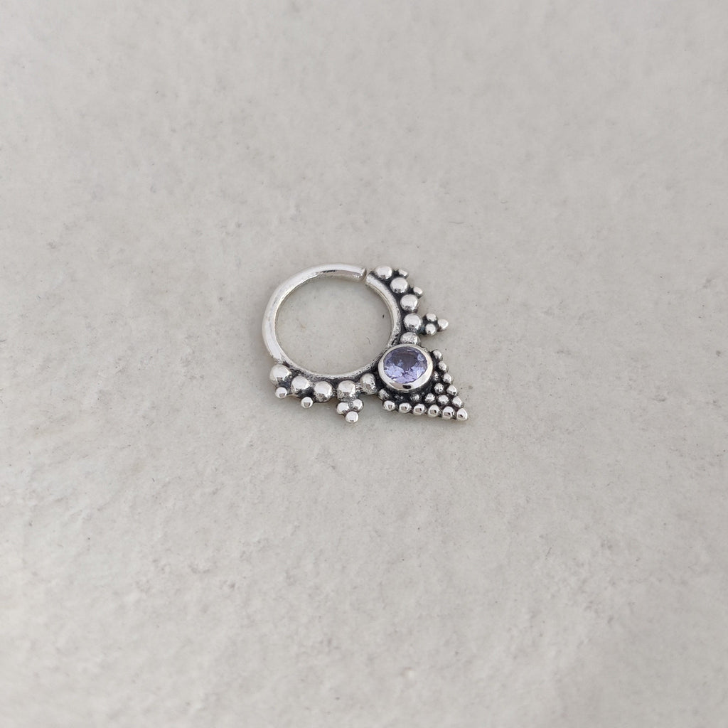 Triangle-shaped silver septum ring with a purple gemstone on a white background