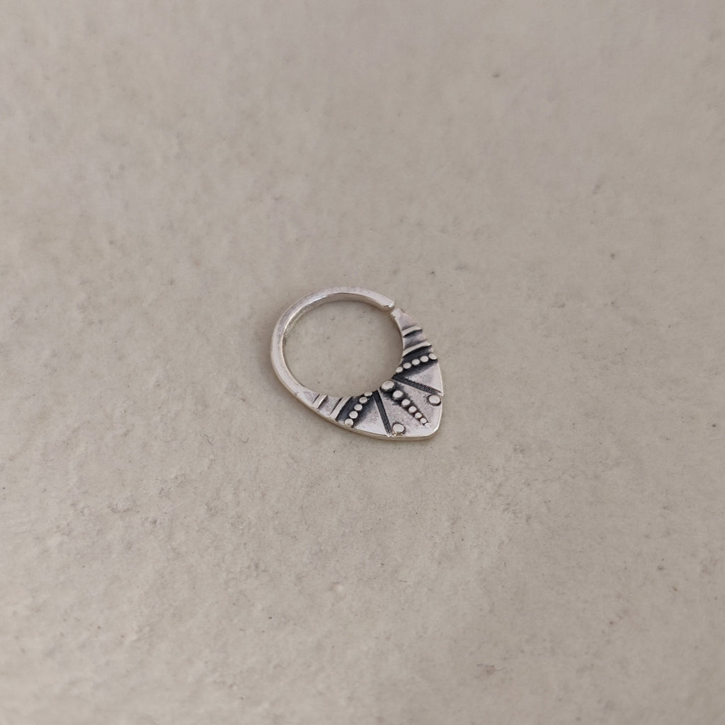 Silver septum nose ring with a geometric design on a textured background.