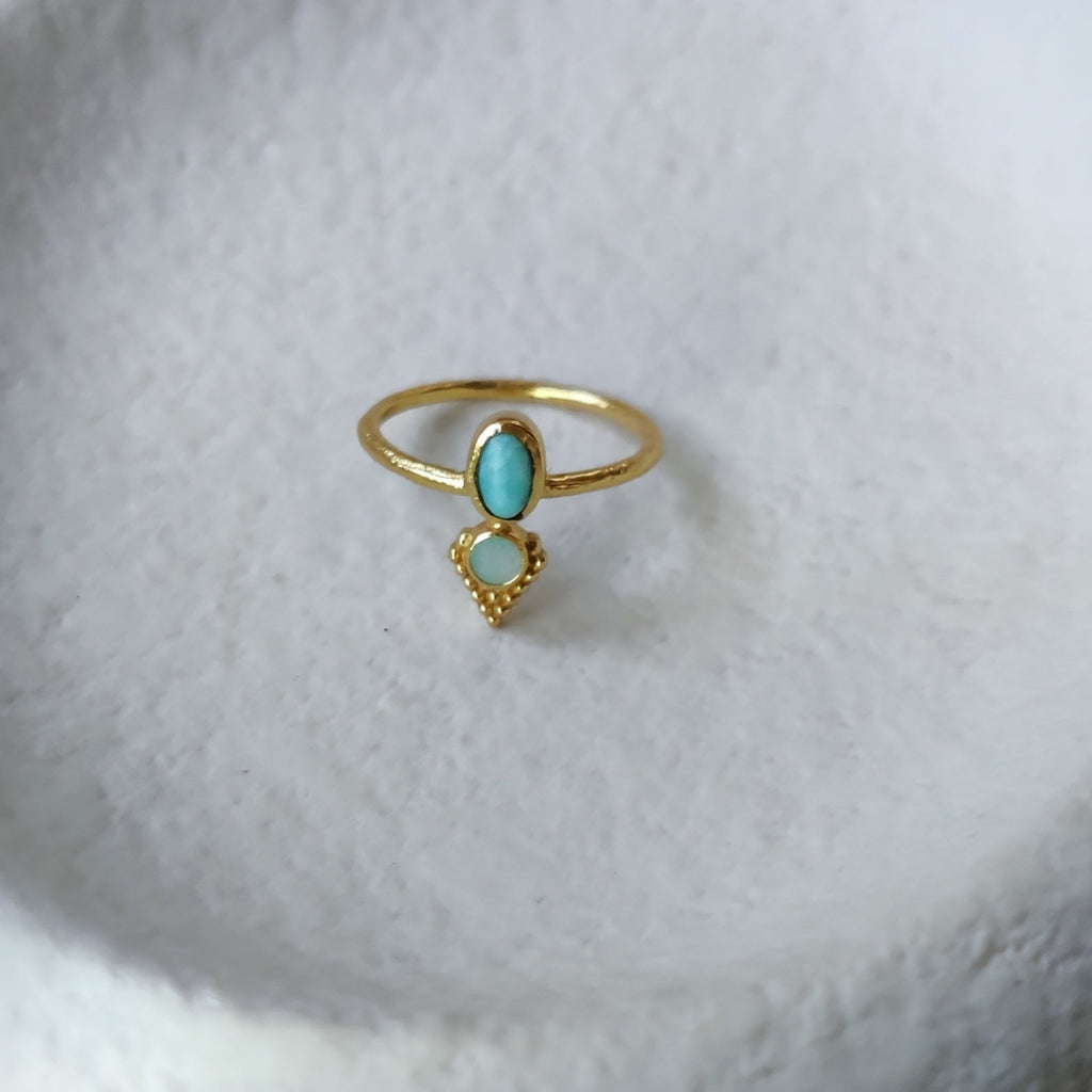 Dainty brass ring with turquoise and abalone shell, displayed on a jewelry plate.