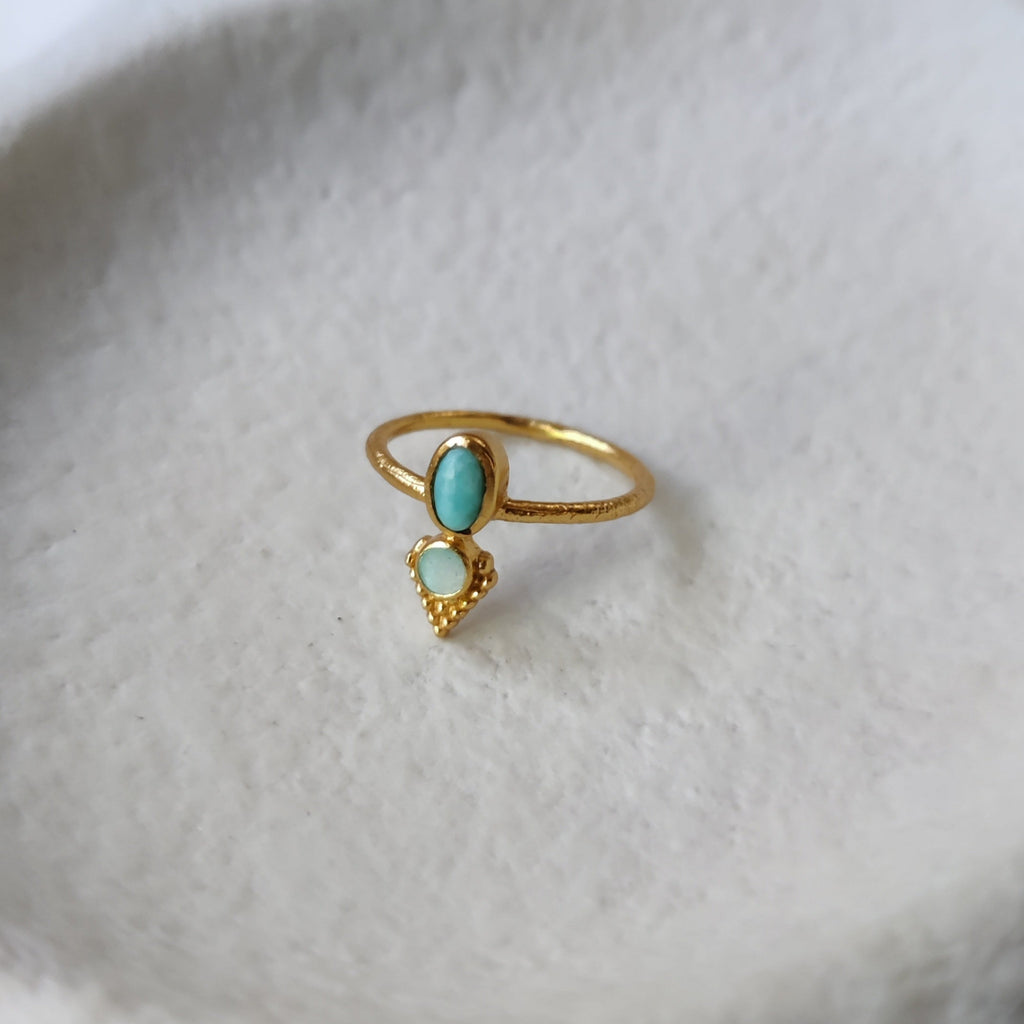 Dainty brass ring with turquoise and abalone shell, displayed on a jewelry plate.