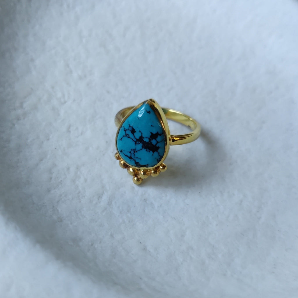 Brass ring with turquoise, displayed on a jewelry plate.