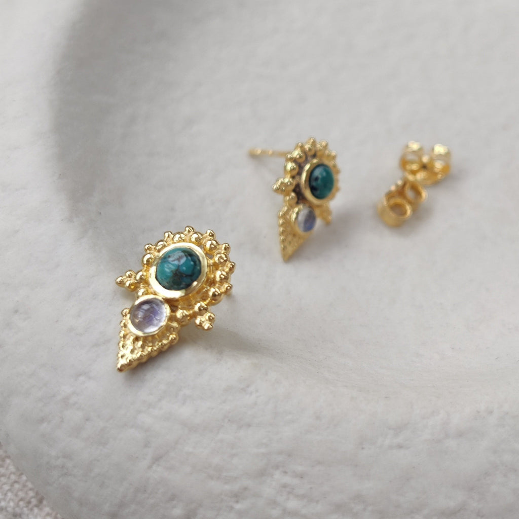 Gold earrings with gemstones on a white stone surface
