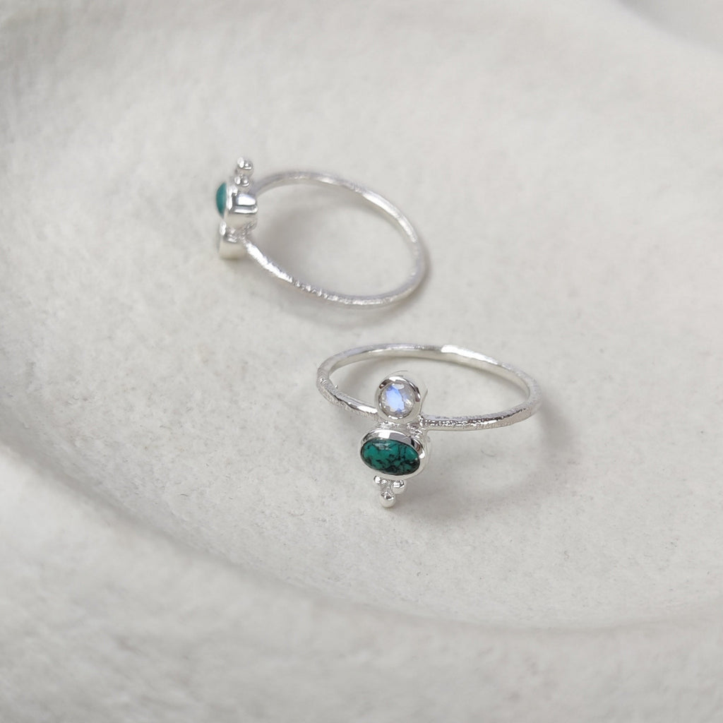 Two silver rings with gemstones on a textured white surface.