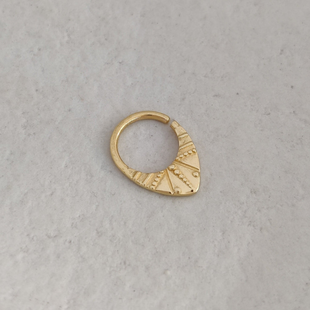 V-shaped gold septum nose ring with intricate design on a textured surface.