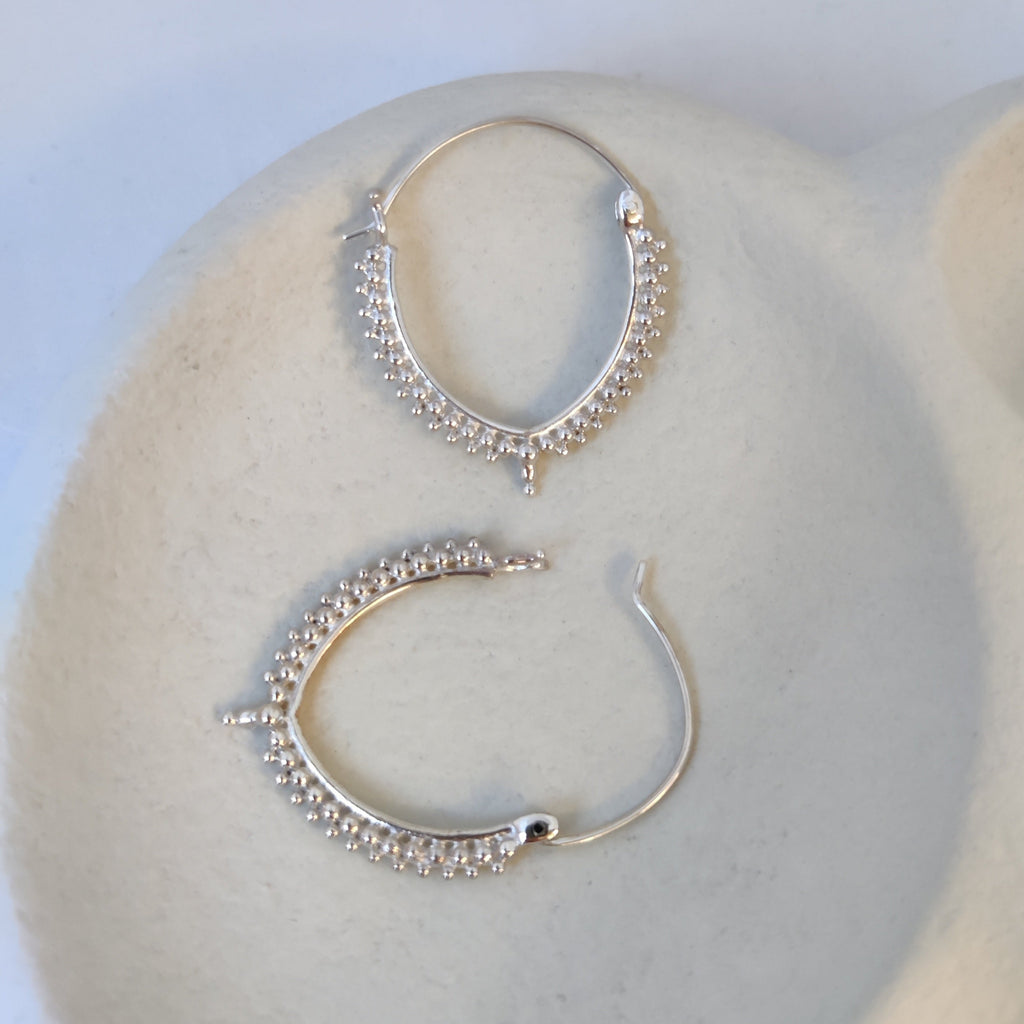 Elegant silver earrings with a subtle V-shape, adorned with delicate dotted details, highlighting their intricate design and open closure mechanism.