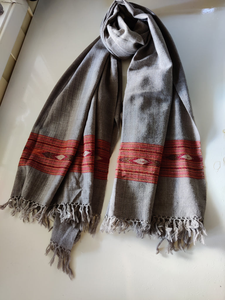 A large wool shawl with beige as the primary color and multicolored geometric patterns, displayed draped on a surface.
