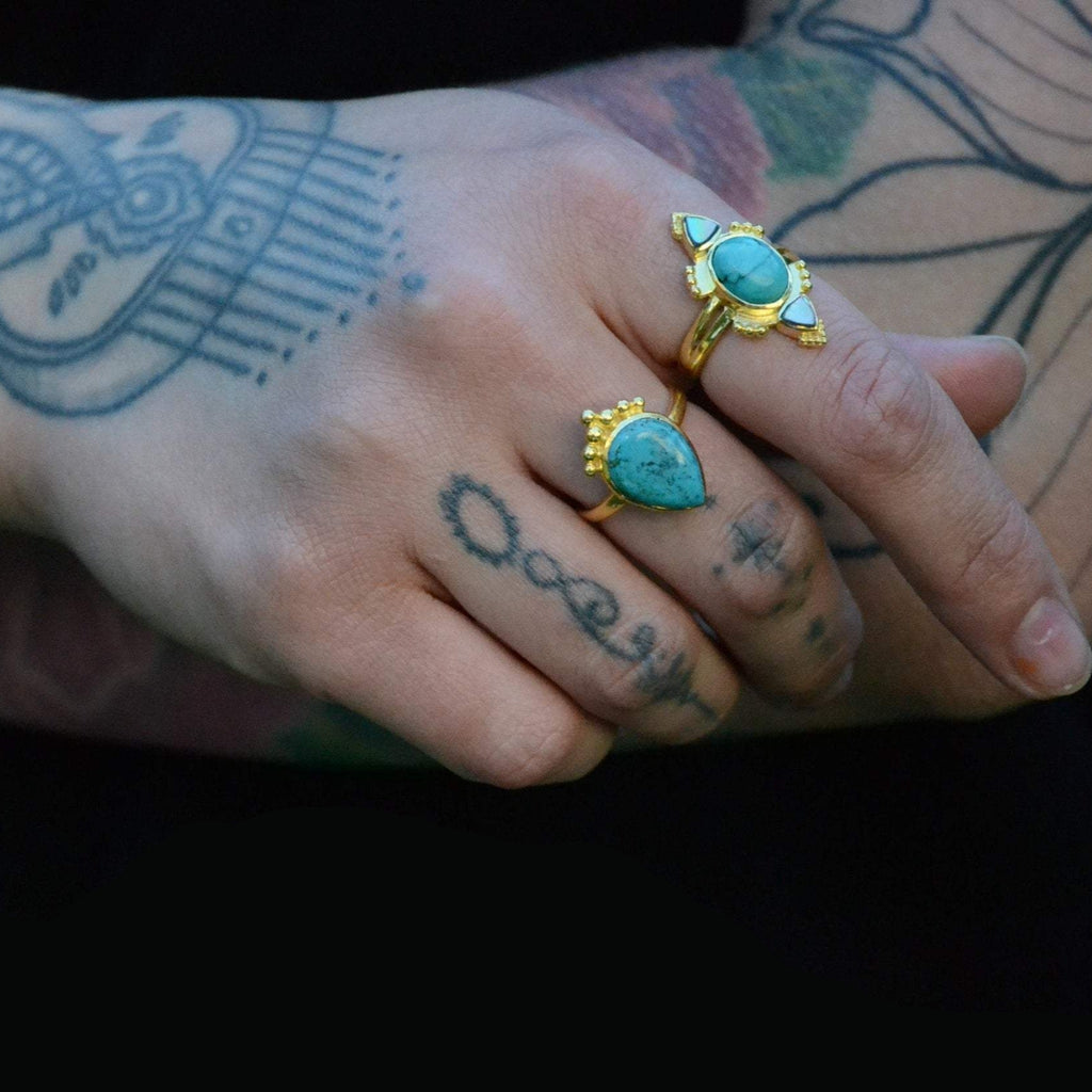 Brass rings with turquoise, worn on a hand.